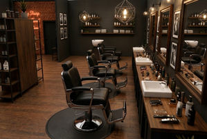 Vue intérieure de l’espace coupe d’un barbershop au style industriel chaleureux, avec fauteuils de barbier noirs, grands miroirs en bois, plan de travail en finition bois et éclairage suspendu contemporain.