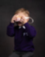 A young boy holds a wooden camera to his face, to take an imaginary photo