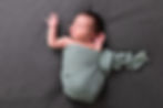 A newborn baby in a sage green wrap, lying on a grey backdrop
