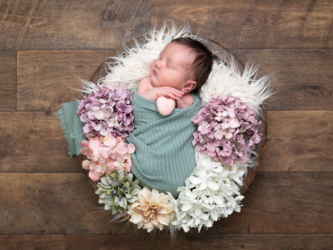 Newborn baby in wooden bowl with flowers