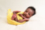 A baby in a yellow wrap is lying on their left side on a white throw