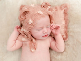Newborn girl with pink bonnet sleeping on pink pillow