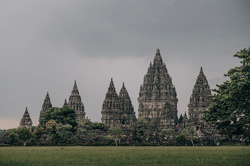 Tempelanlage von Prambanan in Indonesien mit mehreren steinernen Türmen vor bewölktem Himmel.