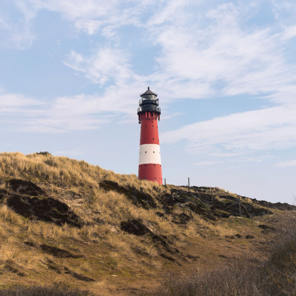 Thumbnail: Leuchtturm Hörnum auf Sylt vor Dünen und blauem Himmel.