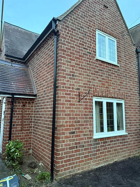Corner of a red brick house with white windows and a black drainpipe fixed to the wall