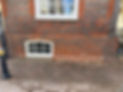 Lower red brick wall with a small arched basement window beneath a larger white sash window