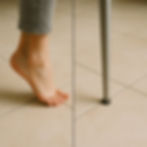 Bare foot on left and chair leg on right, both on tiled floor. Close-up with neutral tones, divided by a line.
