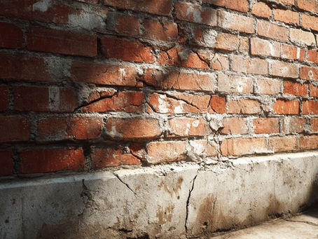 Cracks in a red brick wall near the foundation, showing visible damage caused by moisture and uneven settling