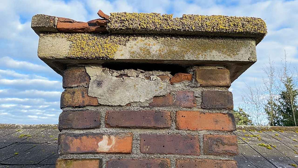 Brick chimney with cracked mortar and mossy bricks under a blue sky with clouds.