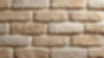 Close-up of a textured beige brick wall with rough surfaces. The bricks are laid in a staggered pattern, creating a rustic appearance.