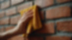 Hand wiping a wet red brick wall with a yellow cloth. Close-up view, focusing on texture and moisture.