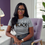 Thumbnail: Woman wearing a white "Minding My Black-Owned Business" t-shirt, while sitting a table
