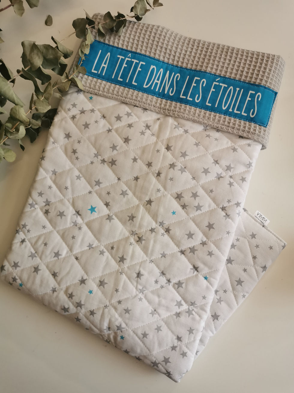 Miniature : Couverture bébé matelassée, recto blanc petites étoiles grises, verso nid d'abeilles gris, appliqué bleu inscription "la tete dans les étoiles" 
