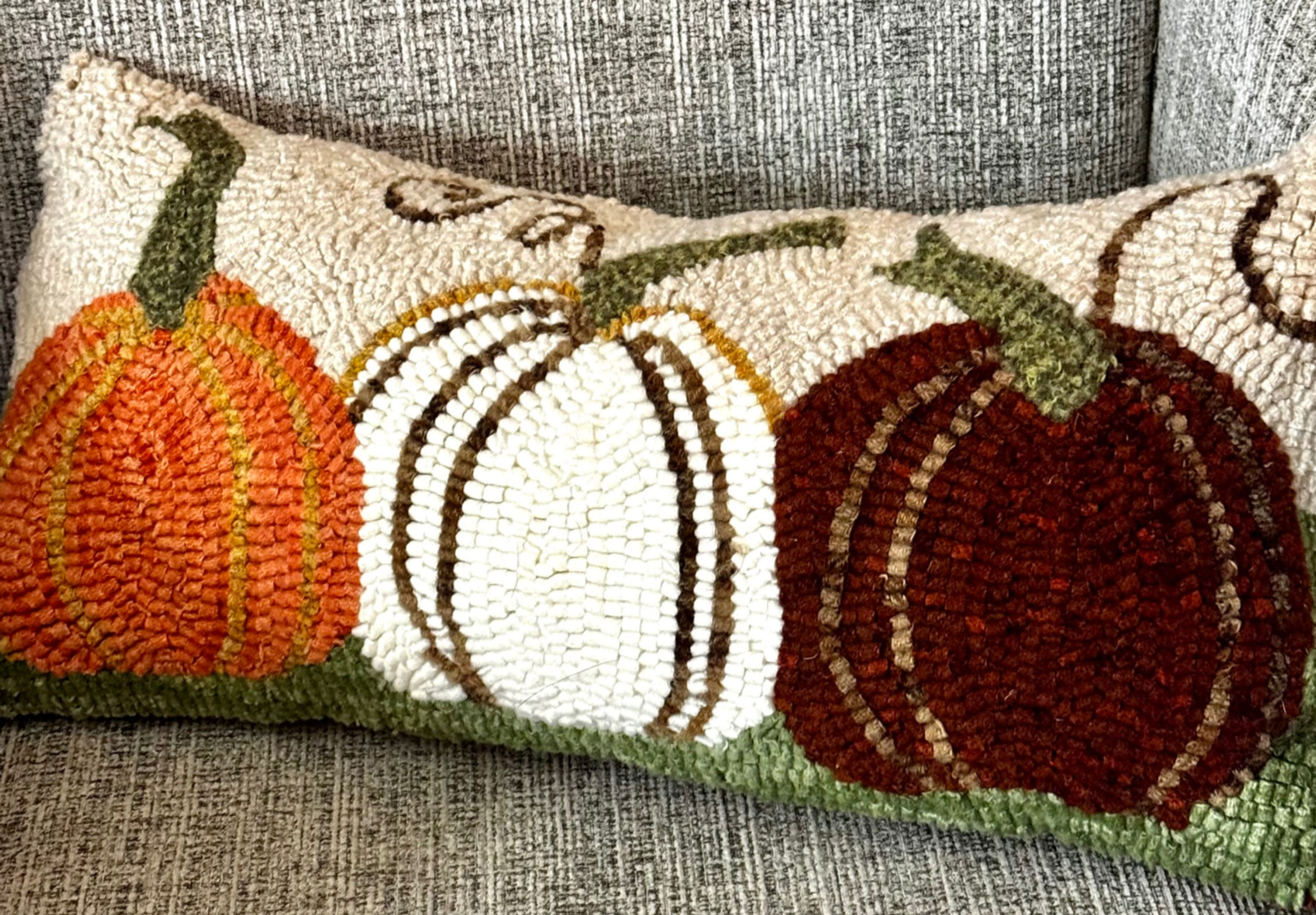 Hand hooked wool bolster pillow of three pumpkins in a chair with hand dyed wool. Orange, white and dark orange and green
