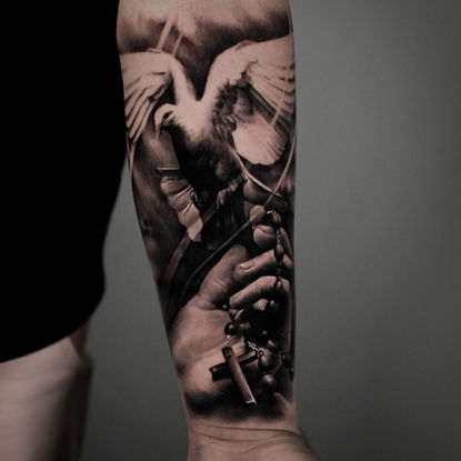 Religiöses Black-and-Grey-Tattoo mit betenden Händen, Rosenkranz und fliegender Taube auf dem Unterarm, tätowiert bei Dado Artist Collective in Arbon und Luzern