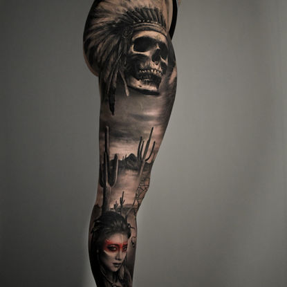 Black-and-Grey-Beintattoo mit Totenschädel im Federschmuck, Wüstenlandschaft und Frauenporträt, gestochen bei Dado Artist Collective in Arbon.
