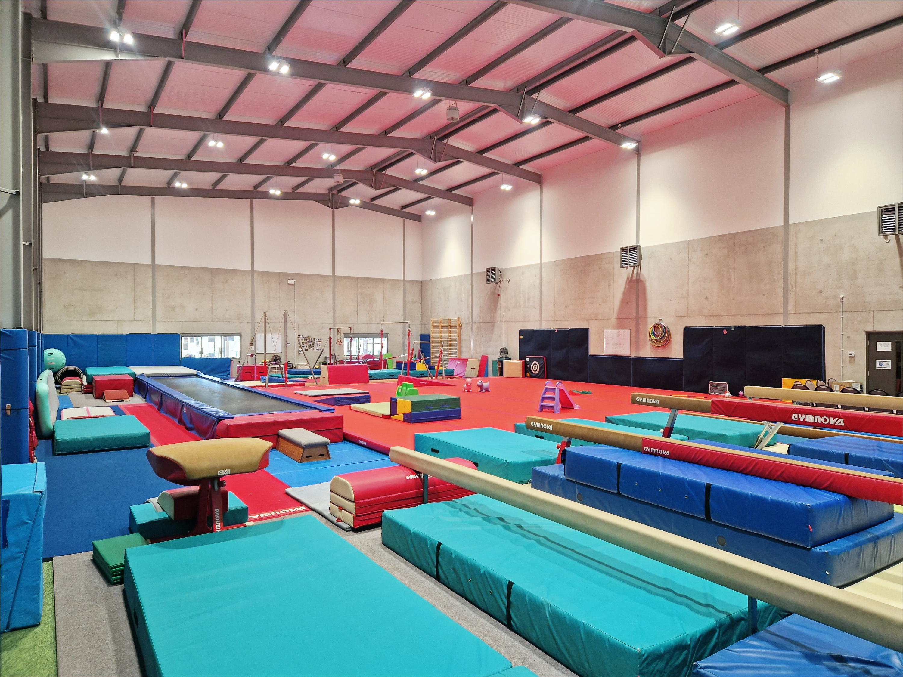 This is an image on the interior of the gym, there is a fast track tumbling and vault area on the left, beams on the right, a sprung floor in the middle and bars at the back, the gym is covered with safety matting.