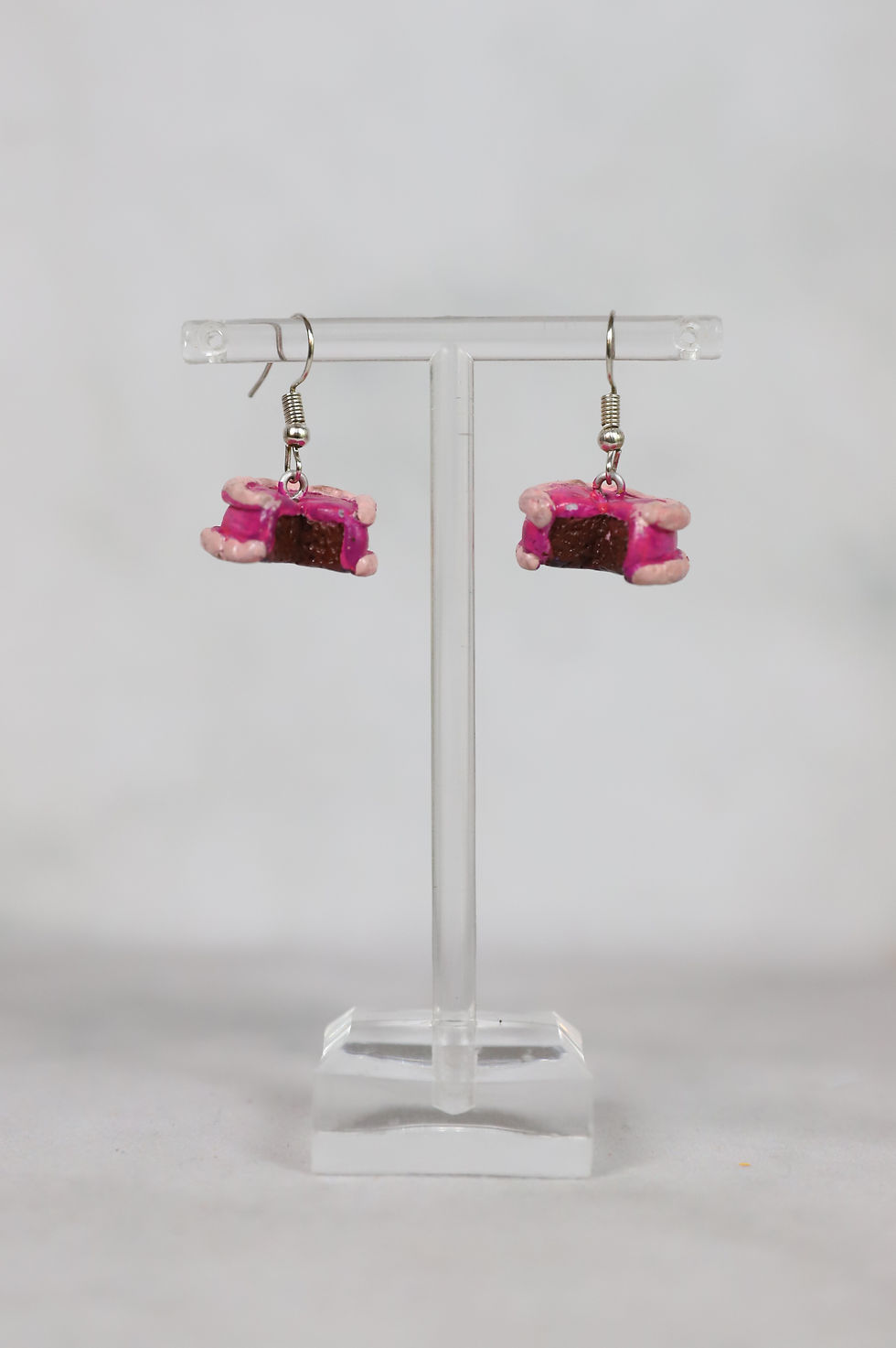 Pink cake slice earrings displayed on a stand