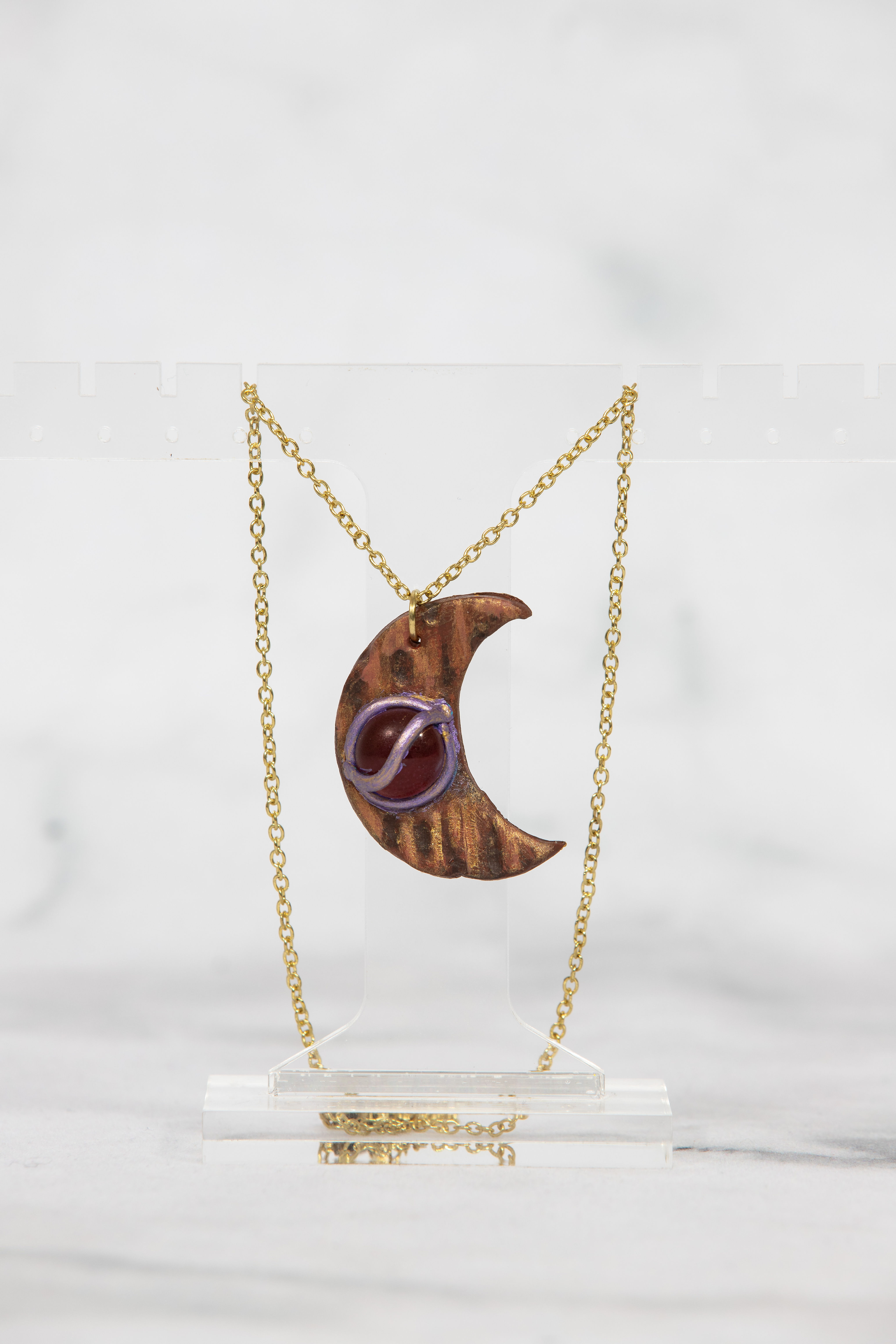 Crescent moon pendant necklace with decorative purple detail and gold chain.