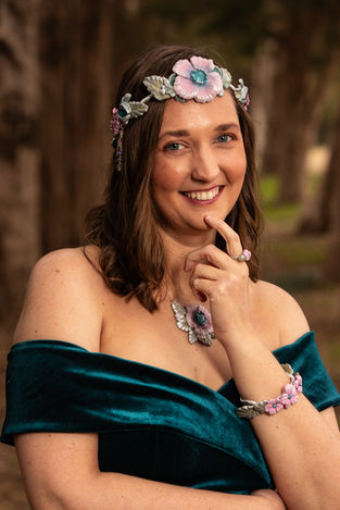 Smiling woman wearing floral crown and jewelry in outdoor portrait setting.