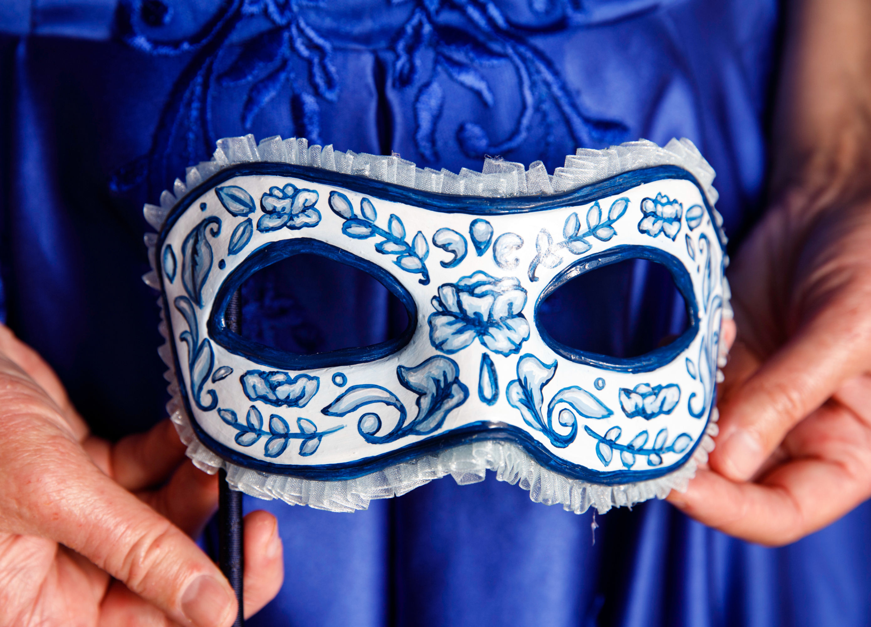 White and blue floral mask held up against a blue fabric background.