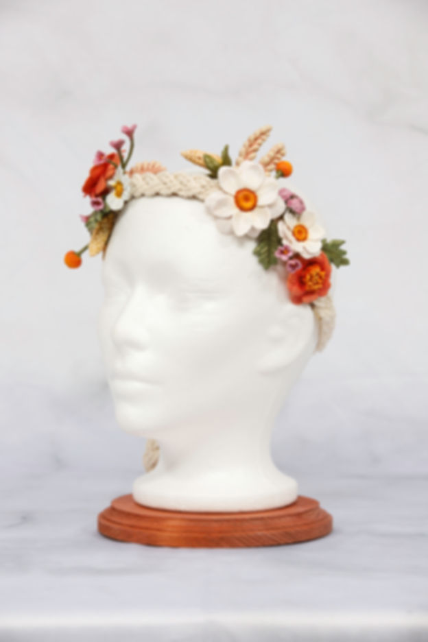 White mannequin head wearing floral crown with daisies and orange flowers.