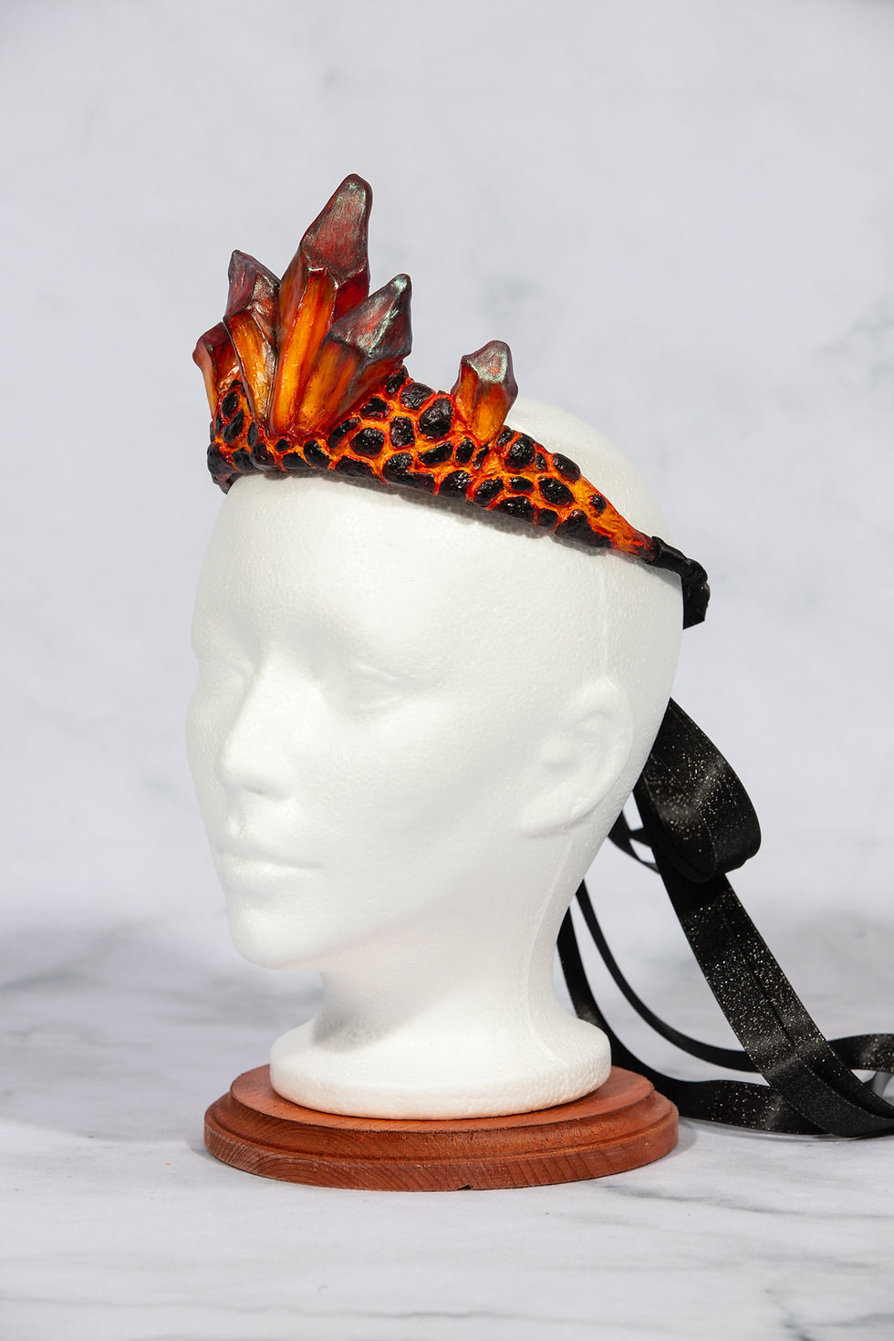 Thumbnail: Orange and black crystal crown on a white head form, studio shot.