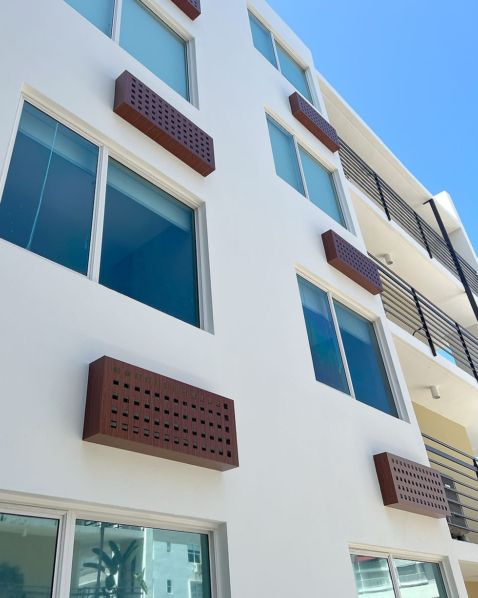 White modern building with blue-tinted windows and wooden brown vent covers. Black railings visible. Clear blue sky in the background.