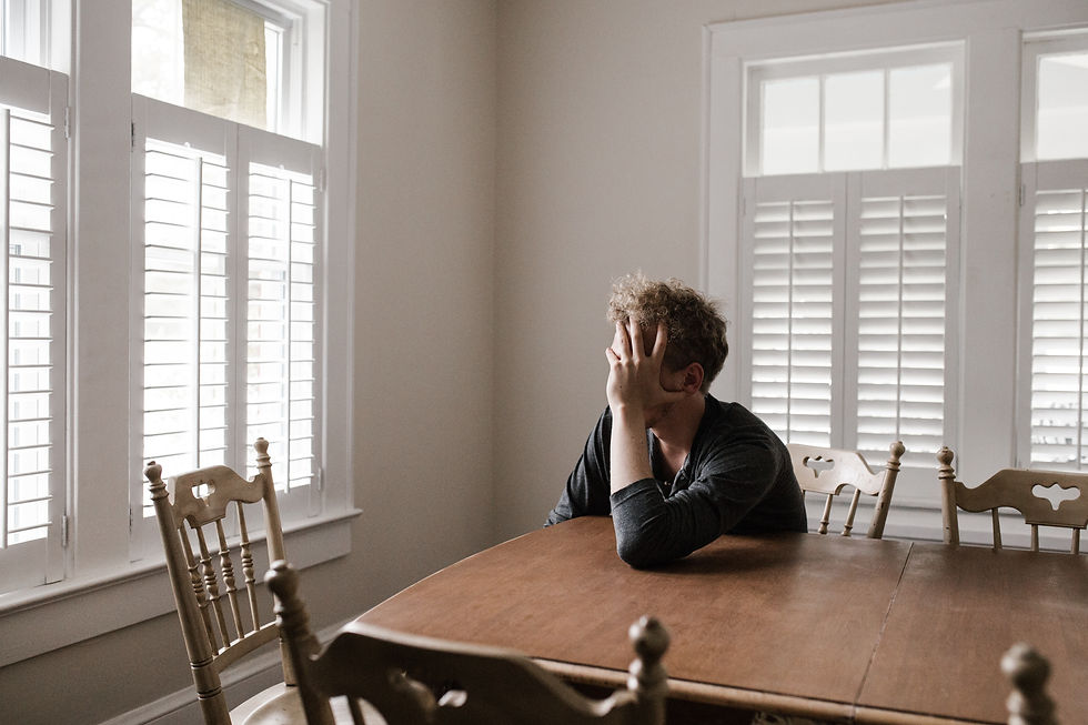 Man sitting at table alone by a window with hand on face to represent frustration in child custody cases