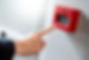 Male hand pointing at red fire alarm switch on concrete wall in office building. Industria