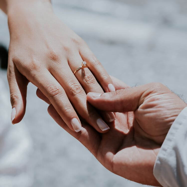 Eine Frauenhand mit Diamant-Ring in gold wird von einer Herrenhand gehalten.