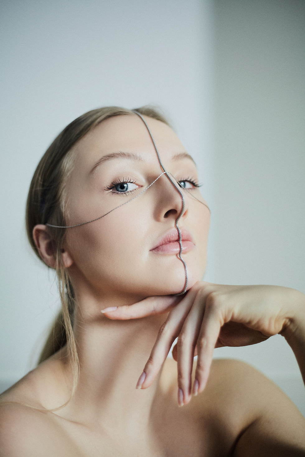 kobieta z dwoma łańcuszkami przecinającymi się na twarzy pozująca do zdjęcia