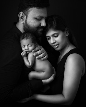 Newborn cuddled between parents in fine art portrait style