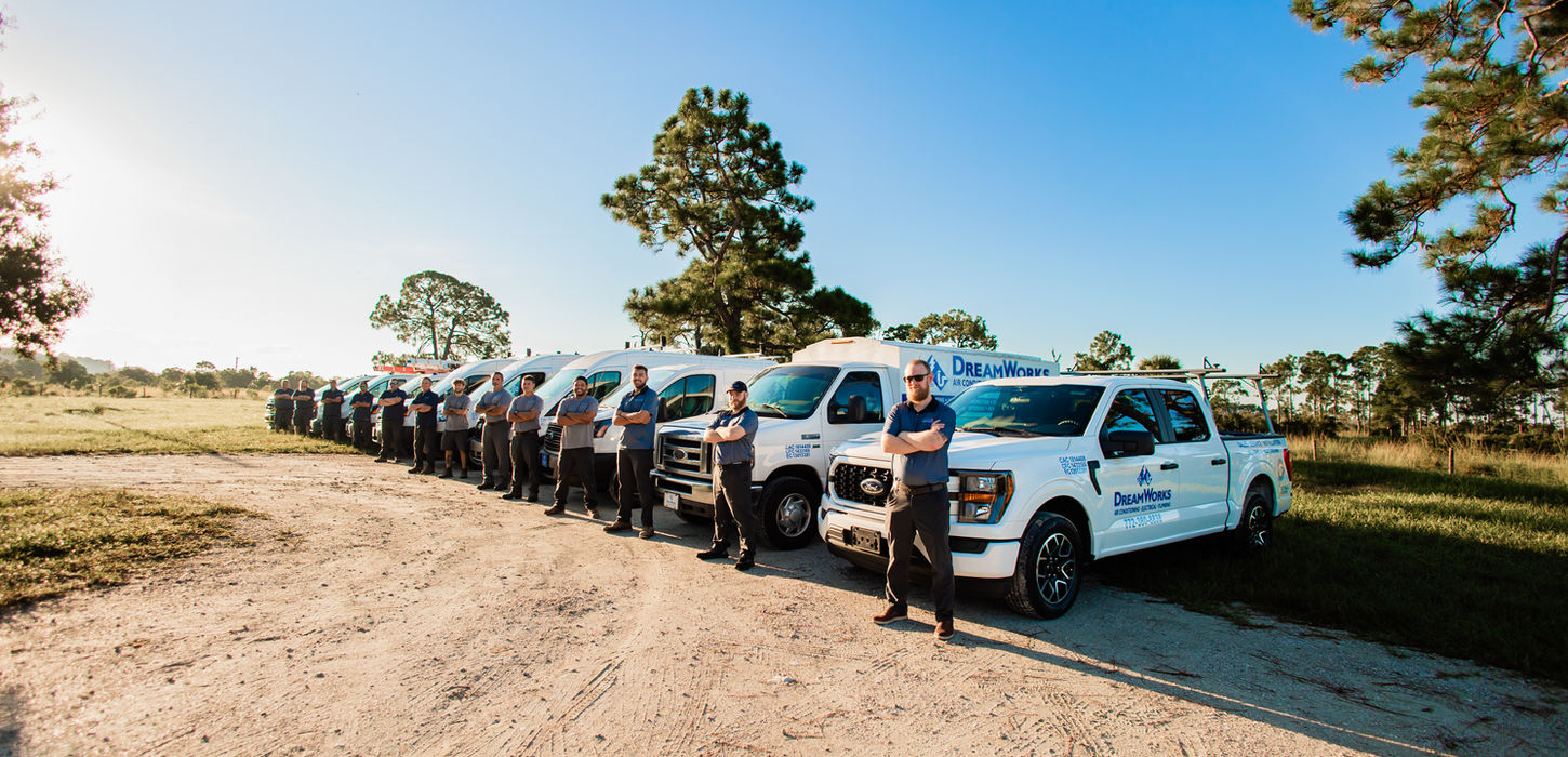 Group of service technicians stand with their trucks on a sunny day.