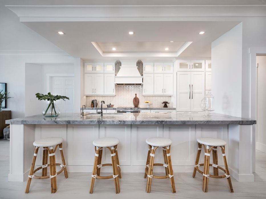 Modern kitchen design with white cabinets with under lights, marble countertop, and bar stools and recessed lighting