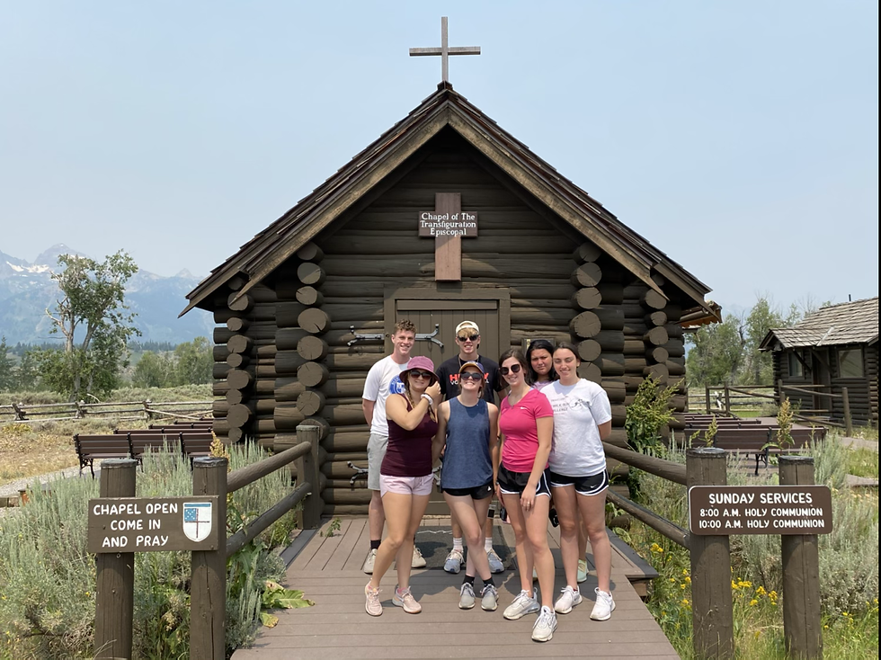 Youth of St. Paul’s stand grouped in front of a wooden chapel building with mountains in the background