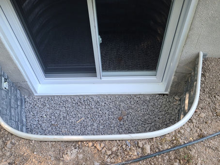 A close-up view of a basement window with an outside view of a metal window well lined with small rocks
