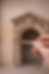 Hand painting a small, ornate beige archway with a detailed face design. The background is textured stone, creating an artistic ambiance.