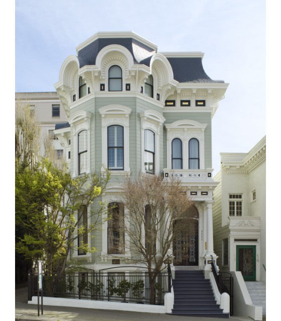 Victorian-style house with ornate details, pale blue facade, and black roof. Surrounded by trees and adjacent to a similar structure. Calm mood.