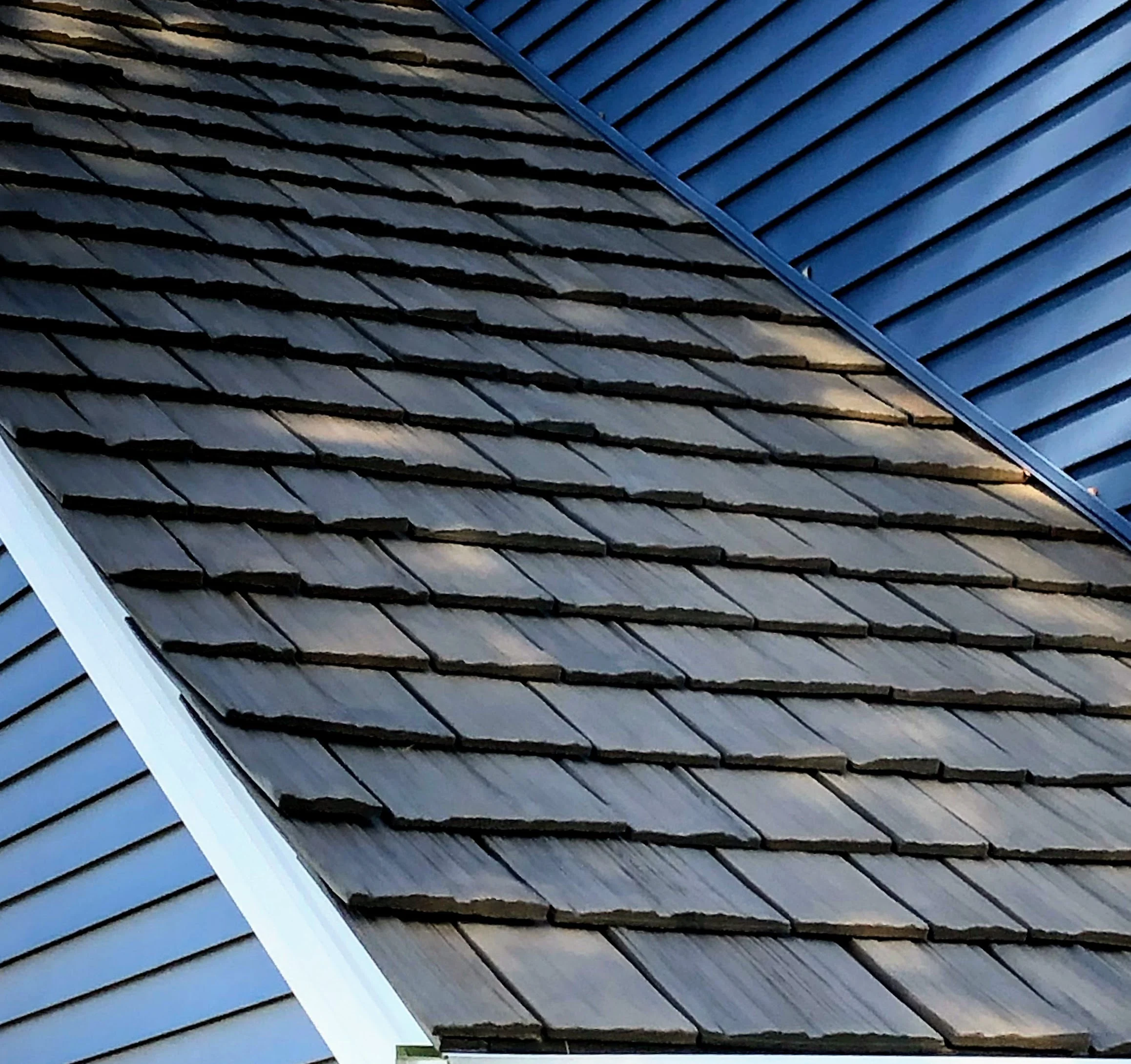 Close-up of a synthetic shake roof against blue siding, highlighting the realistic wood texture, superior durability, and weather resistance.