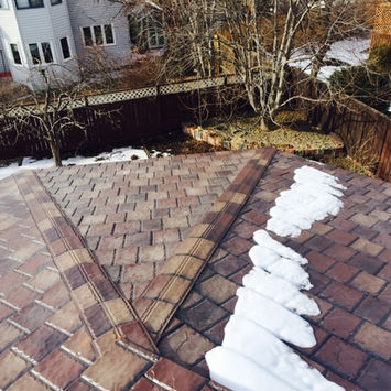 An older asphalt shingle roof with moss growth and partial snow coverage.