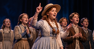 Young performers in period costumes singing on stage in a production of Anne of Green Gables.