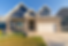 Modern suburban house with stone facade, two gables, white garage door, and green lawn. Bright blue sky creates a welcoming mood.
