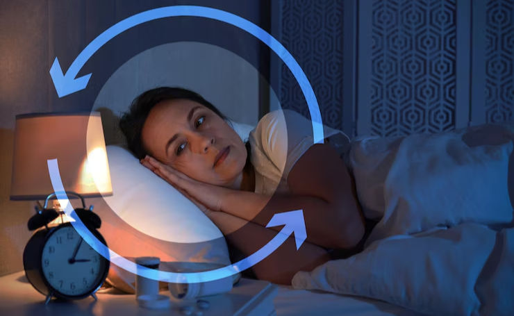 Woman in bed, unable to sleep, looks pensive. Alarm clock, lamp on bedside table. Blue circular arrows overlay, suggesting insomnia cycle.