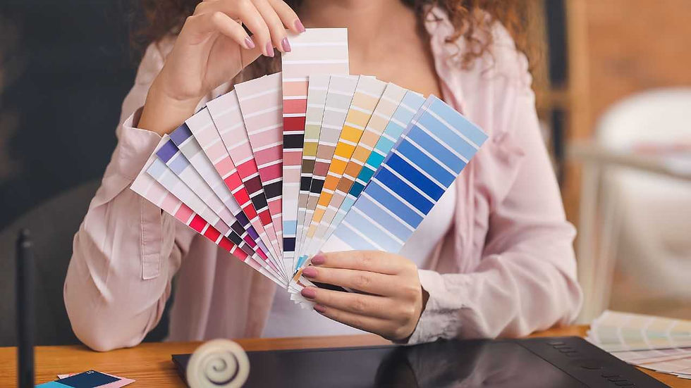 Person holds a colorful fan of paint swatches in a bright setting. The swatches include pink, blue, and yellow hues. Cozy mood.