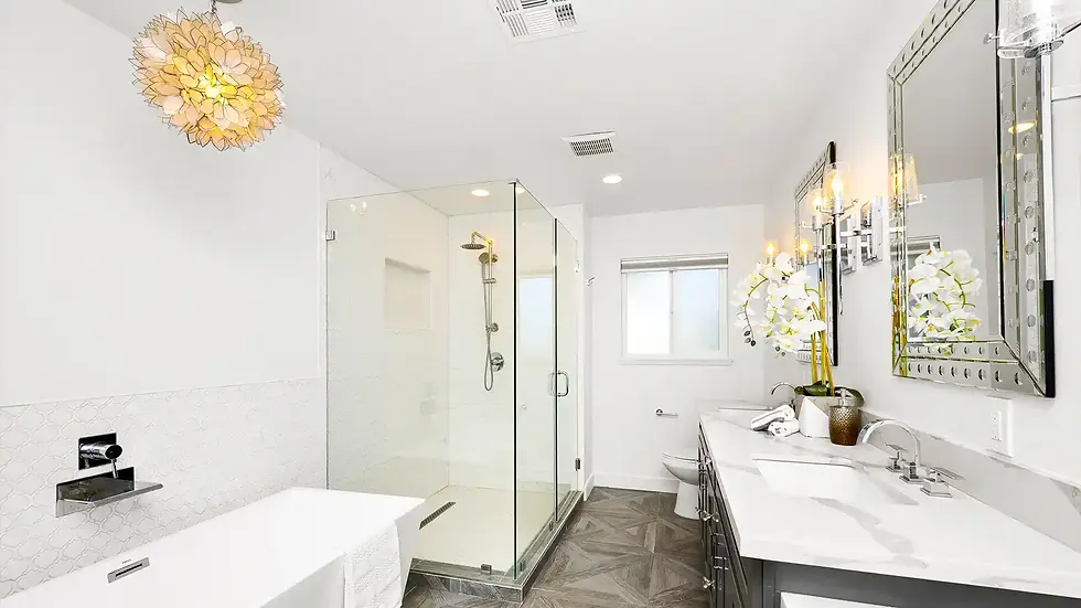 Modern bathroom with glass shower, white tub, and dual sinks on a marble counter. Floral decor and a chandelier create an elegant mood.