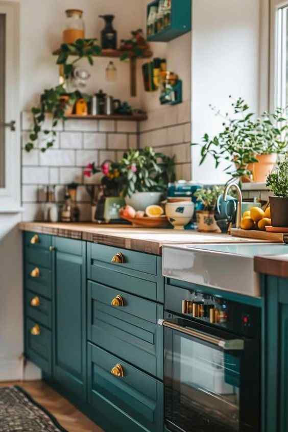 Cozy kitchen with teal cabinets, brass handles, and wooden countertop. Potted plants and lemons near a window; cheerful ambiance.