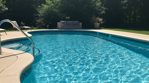 Sunny pool scene with clear blue water, patio furniture, and plants. Surrounded by greenery, creating a calm and inviting atmosphere.