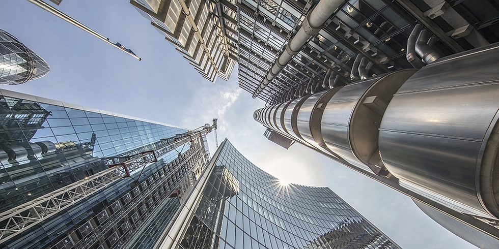 Looking up at modern skyscrapers in a city with glass and metallic facades, under a clear blue sky and bright sunlight.