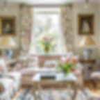 Elegant living room with floral decor; pink sofa, floral curtains, colorful cushions, and table with flowers. Sunlit window and portrait paintings.